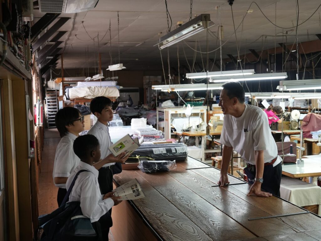 工場の作業台の前で、説明を聞く南河原中学校の生徒の皆さん