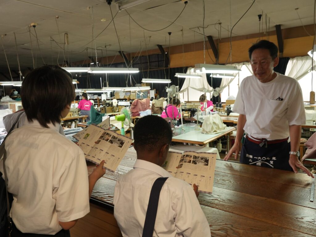 工場の中で、冊子を見ながら説明を聞く南河原中学校の生徒の皆さん